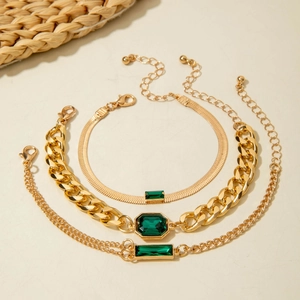 Detailed view of three-piece gold layered bracelets with emerald green faux gemstones