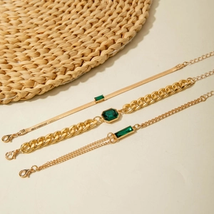 Detailed view of three gold layered bracelets featuring emerald green gemstones