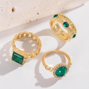Détail de trois bagues dorées avec pierres d'émeraude et accents de diamant sur pierre