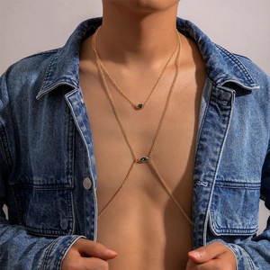 Detail of trendy gold body chain with faux emerald stones and hollow heart pendant