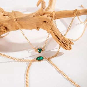 Detail of gold chain necklace featuring heart and marquise cut green gemstones on wood