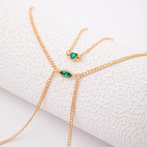 Detail of gold body chain featuring green emerald heart and marquise cut pendants