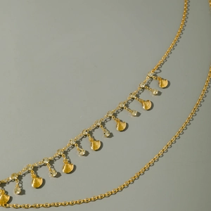 Close-up of golden body chain featuring engraved shell pendants and round crystal accents