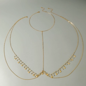 Detail of gold body chain featuring shell charms and faux emerald rhinestones on grey