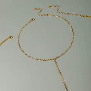 Gold Y-shaped body chain with emerald-style heart pendant and lobster clasp on dark base