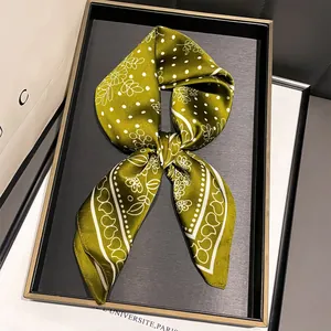 Dettaglio di un foulard in seta verde oliva con motivo paisley annodato su un vassoio