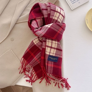 Close-up of red and white plaid scarf with fine fringe and woven label on beige coat