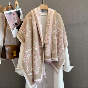 Detail of floral jacquard scarf with soft tassels draped over a white wool coat