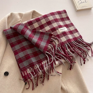 Detail of red and grey plaid scarf with fringes and elegant label on a beige wool coat