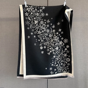 Détail d'une écharpe noire avec motifs floraux blancs et finitions à franges