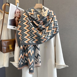 Detail of zigzag jacquard knit scarf with fringe ends draped over a white wool coat