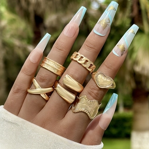 Detailed view of a 7-piece set of gold geometric rings worn on a hand in natural light