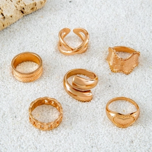 Close-up of a 6-piece gold-plated ring set with wave and heart designs on white sand