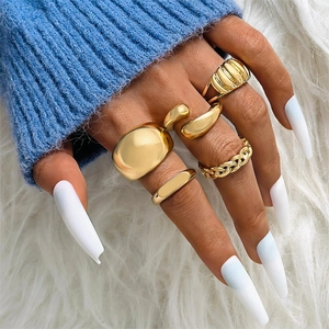 Five-piece gold geometric ring set styled on a hand with blue knitwear and plush background