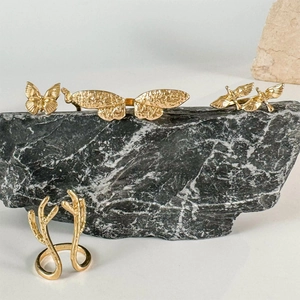 Detailaufnahme goldener Schmetterlings- und Geweihringe auf schwarzem Steinhintergrund