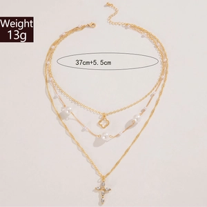 Detail einer mehrlagigen Goldkette mit Kleeblatt-Anhänger, Perlen und einem Strass-Kreuz