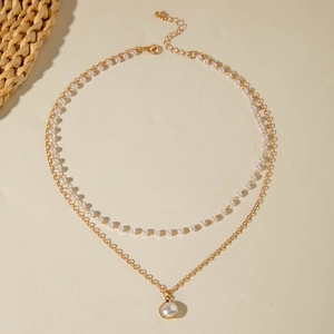 Elegante zweilagige Halskette mit weißen Perlen und goldenem Anhänger auf warmem Hintergrund