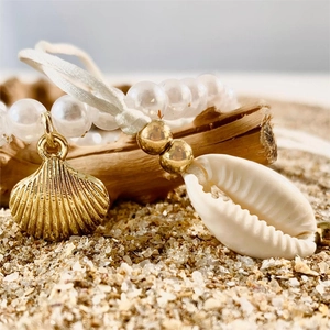 Macro detail of beach style shell and pearl bracelet on a piece of driftwood over sea sand