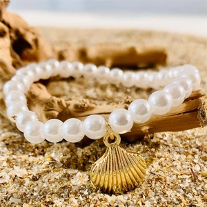 Close-up of pearl beach bracelet with golden shell charm on sand and driftwood