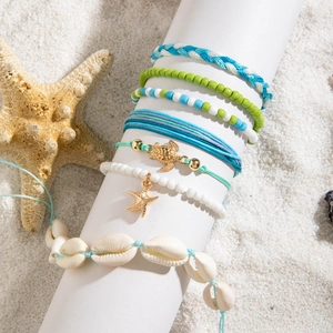 Detail of seven bohemian ocean-themed bracelets with shells and starfish on white sand
