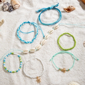 Flat lay of beach shell bracelets with starfish and turtle charms on white sand