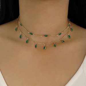 Close-up of a double-layer gold necklace with green teardrop gemstones on a model