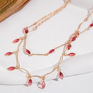 Detail view of gold layered necklace with pink marquise-cut pendants on white stone