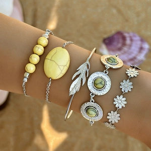 Close-up of Bohemian layered bracelets with turquoise stones and feather charm on a beach