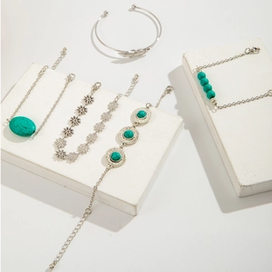Close-up of bohemian silver feather bangle and turquoise floral bracelets on white blocks