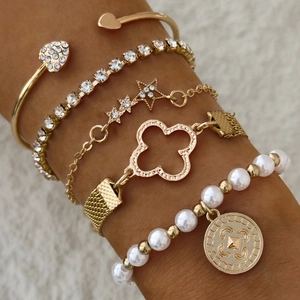 Détail de bracelets dorés superposés avec trèfle et pièce en perle sur le poignet