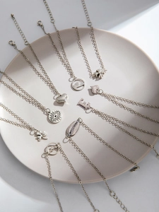 Detailed view of assorted silver alloy anklets with charm pendants in a ceramic tray