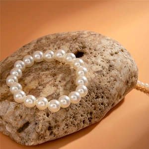 Elegant single strand white round pearl bracelet on textured natural stone background