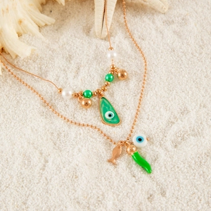 Layered gold evil eye necklace with chili and fish charms on white beach sand