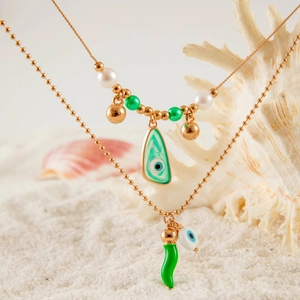 Detail of gold beach necklaces with green chili and evil eye charms on white sand