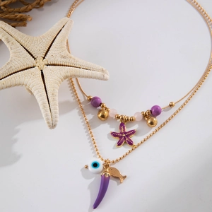 Close-up of beach necklaces with sea star and evil eye charms on golden bead chains