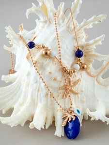 Detail of beaded necklace with starfish, palm leaf and blue drop pendant on a conch