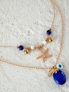 Detail of bohemian gold layered necklace with starfish and evil eye charms on white sand