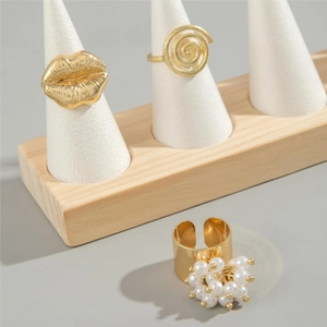 Close-up of gold-plated rings set featuring lip shape, spiral, and pearl details on stands