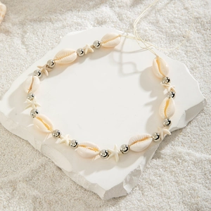 Close-up of beach body chain with natural cowrie shells and silver starfish on white stone