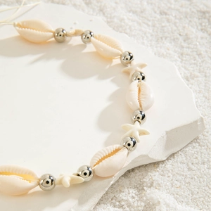 Macro detail of beach style shell waist chain with starfish charms on sand and stone