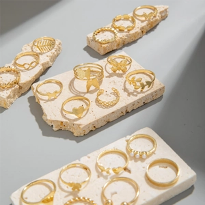 Detailansicht eines 16-teiligen Goldring-Sets mit Schmetterlings- und Herzmotiven auf Stein
