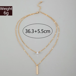 Detail of layered gold Y-necklace with teardrop pendant and rectangle bar charm
