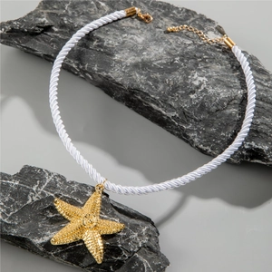 Detail of golden starfish pendant on white braided rope necklace over gray stones