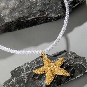 Detailed macro view of textured gold starfish pendant on a white twisted cord necklace