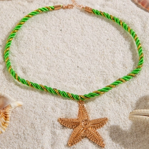 Macro detail of a textured gold starfish pendant on a green braided cord over white beach sand