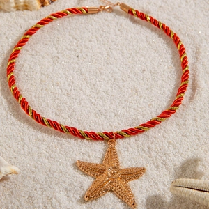 Golden starfish pendant necklace with red braided cord on white beach sand