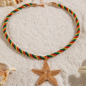 Detailed macro of gold starfish pendant on beach sand with woven rope and metal clasp