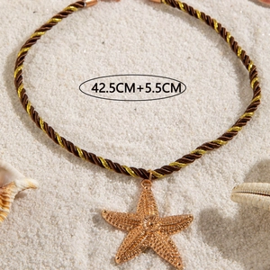 Detailed view of golden starfish pendant with woven rope on white sand and seashells