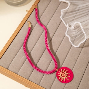 Detail of rose pink woven cord necklace featuring a gold spiral sun pendant on grey tray