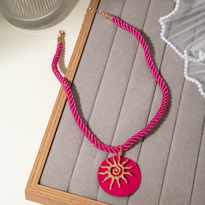 Detail of magenta rope necklace with gold sun pattern pendant on a velvet tray